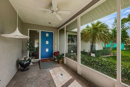 A covered porch features a blue front door, a ceiling fan, and a screened-in view — 4577 GREAT LAKES DRIVE S UNIT 1, CLEARWATER, FL