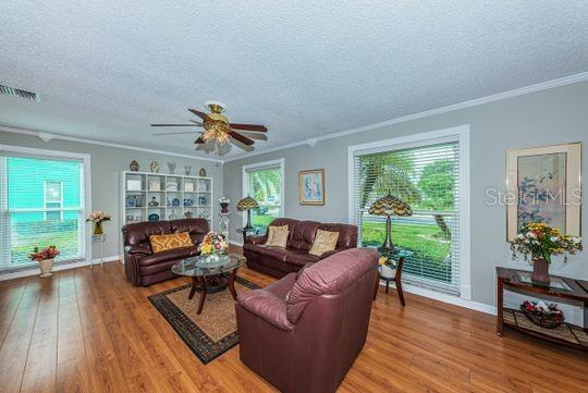 A living room features wood-look flooring, a ceiling fan, leather furniture, and large windows — 4577 GREAT LAKES DRIVE S UNIT 1, CLEARWATER, FL