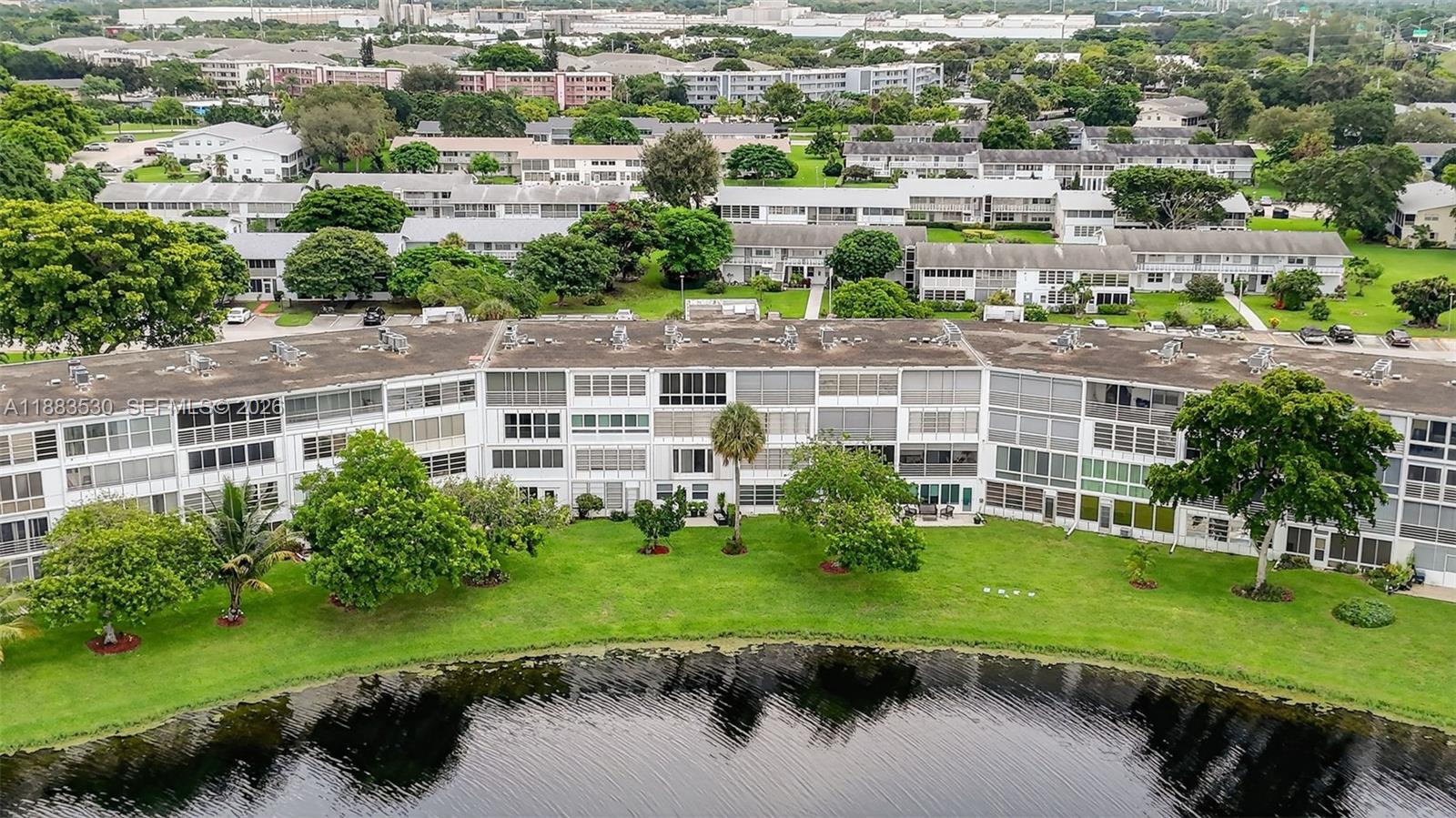 An aerial view shows a multi-story apartment building situated beside a lake and green lawn — 2009 N Farnham  N # 2009, Deerfield Beach FL 33442, DEERFIELD BEACH, FL