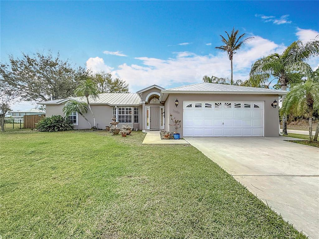 A single-story house with a white metal roof, beige stucco exterior, and a two-car garage — 2686 SW FAIRGREEN ROAD, PORT ST LUCIE, FL