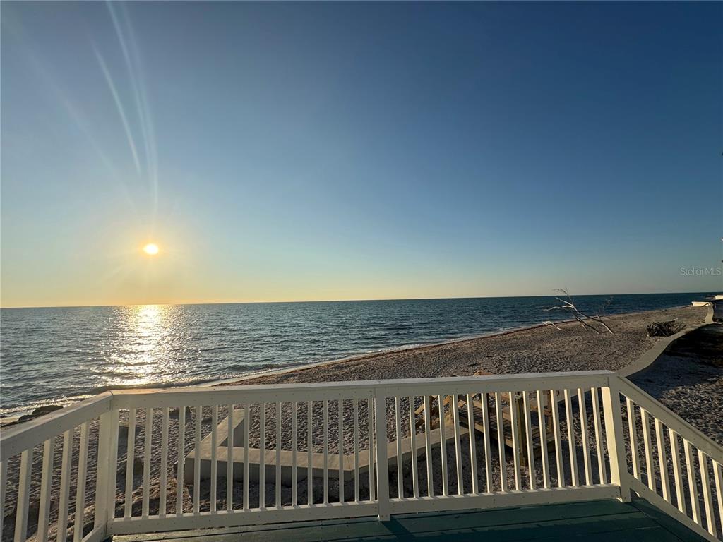 A white wooden deck railing overlooks a sandy beach and the ocean at sunset — 7090 MANASOTA KEY ROAD, ENGLEWOOD, FL