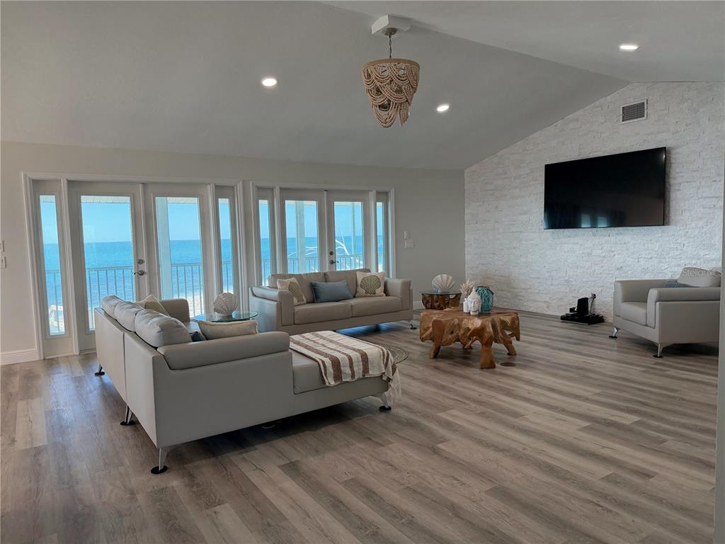 A living room features light wood floors, a white brick wall, and ocean-view glass doors — 7090 MANASOTA KEY ROAD, ENGLEWOOD, FL