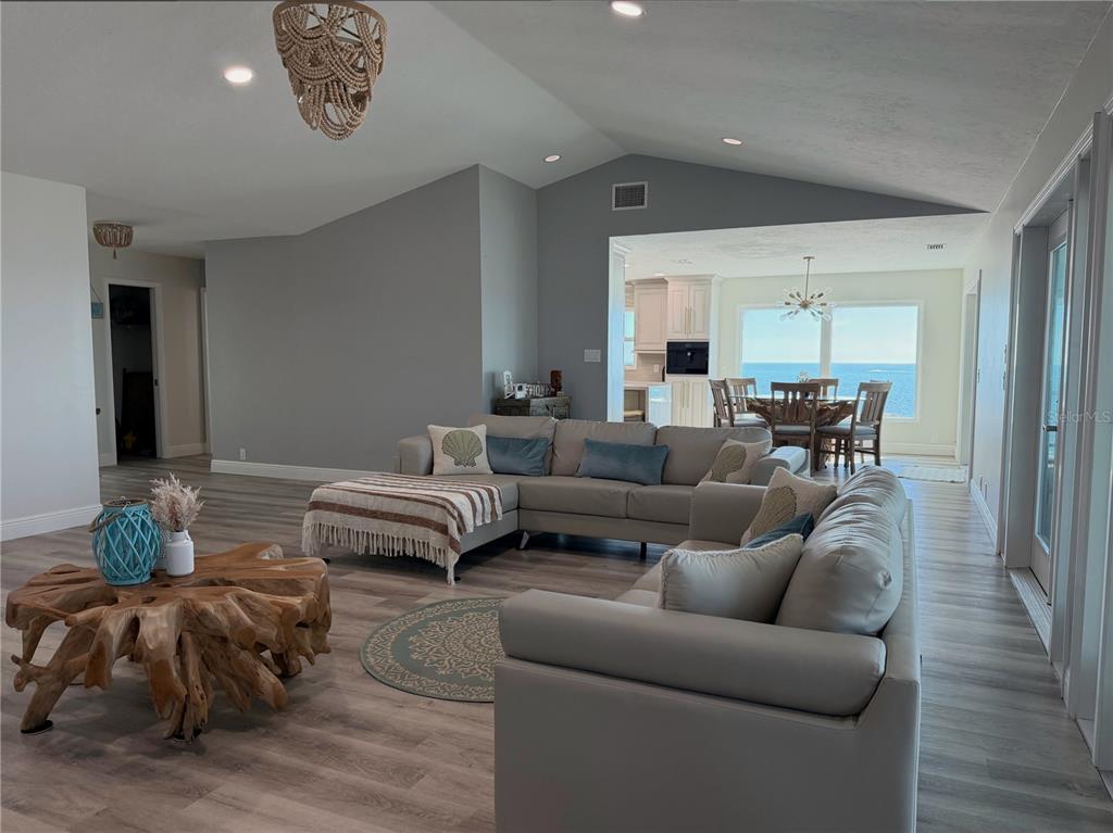 A living room with a sectional sofa, wood root coffee table, and ocean view dining area — 7090 MANASOTA KEY ROAD, ENGLEWOOD, FL