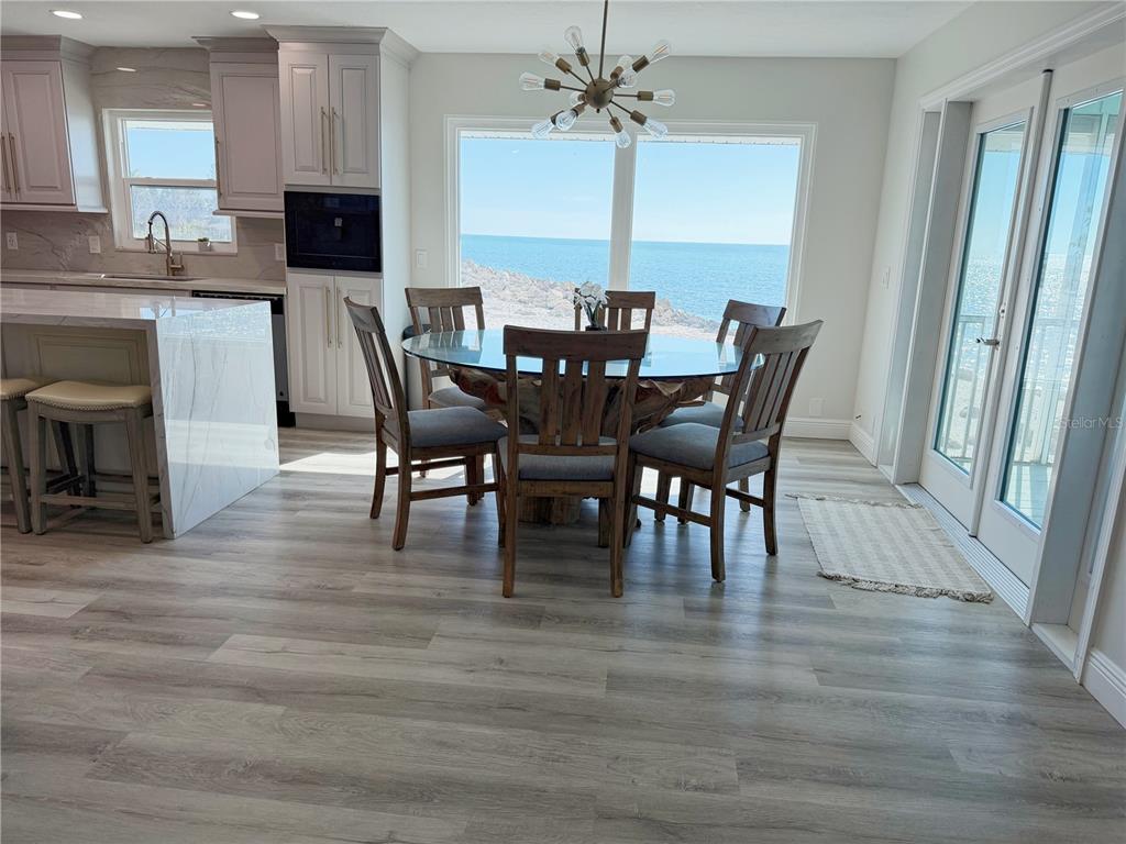 A dining area with a glass table and ocean view sits beside a modern kitchen — 7090 MANASOTA KEY ROAD, ENGLEWOOD, FL