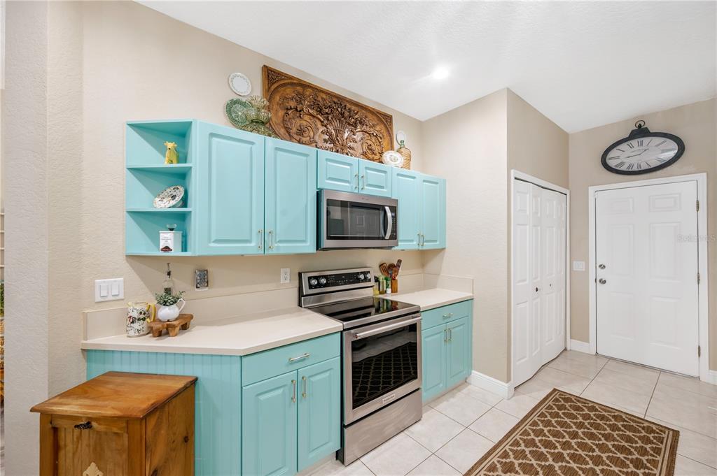 A kitchen features bright turquoise cabinets, stainless steel appliances, and a view into the living area — 11517 CAPTIVA KAY DRIVE, RIVERVIEW, FL
