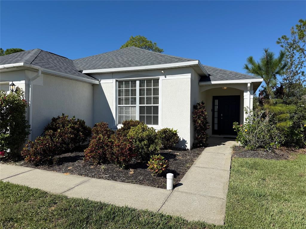 The exterior of a single-story house features a light-colored stucco facade, a gray roof, and landscaping — 1529 GULF VUE DRIVE, HAINES CITY, FL