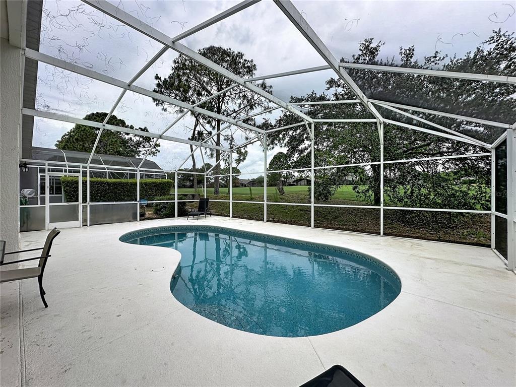 A kidney-shaped swimming pool sits inside a screened-in patio overlooking a grassy golf course — 1529 GULF VUE DRIVE, HAINES CITY, FL