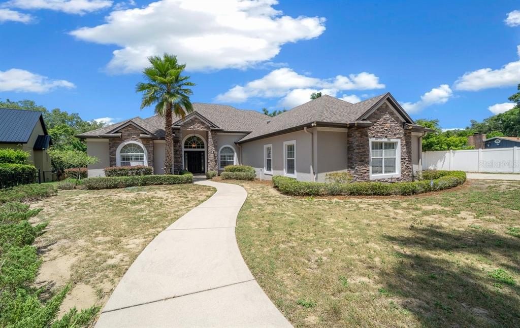A single-story house with stone accents, a concrete walkway, and a palm tree in front — 1251 MAGNOLIA FARMS COURT, EUSTIS, FL