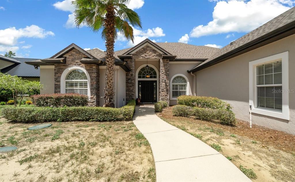 A single-story house with a stone facade, arched windows, and a concrete walkway — 1251 MAGNOLIA FARMS COURT, EUSTIS, FL