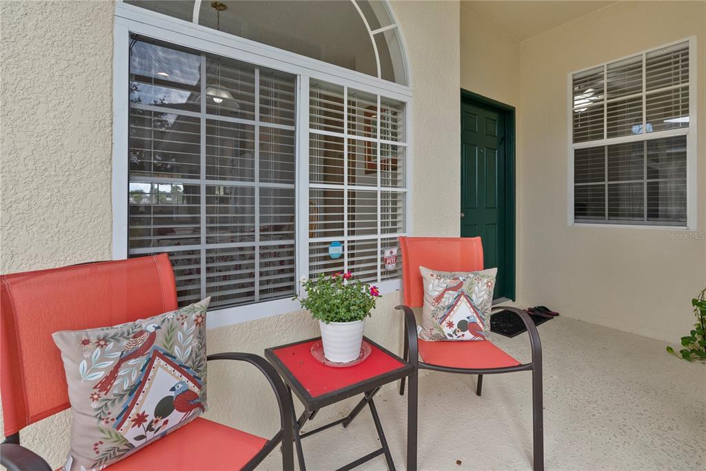 A covered patio features two orange chairs, a small table with a plant, and windows — 104 CLUB VILLAS LANE UNIT N/A, KISSIMMEE, FL