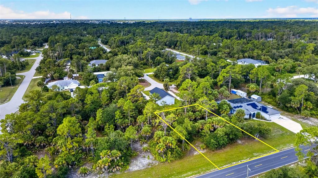 An aerial view shows a vacant, wooded residential lot outlined in yellow along a paved road — 18303 HILLSBOROUGH BOULEVARD, PORT CHARLOTTE, FL