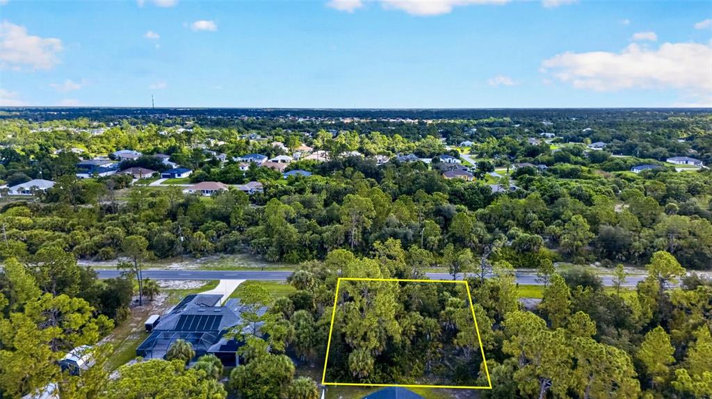 An aerial view shows a vacant, wooded lot outlined in yellow near a paved road — 18303 HILLSBOROUGH BOULEVARD, PORT CHARLOTTE, FL