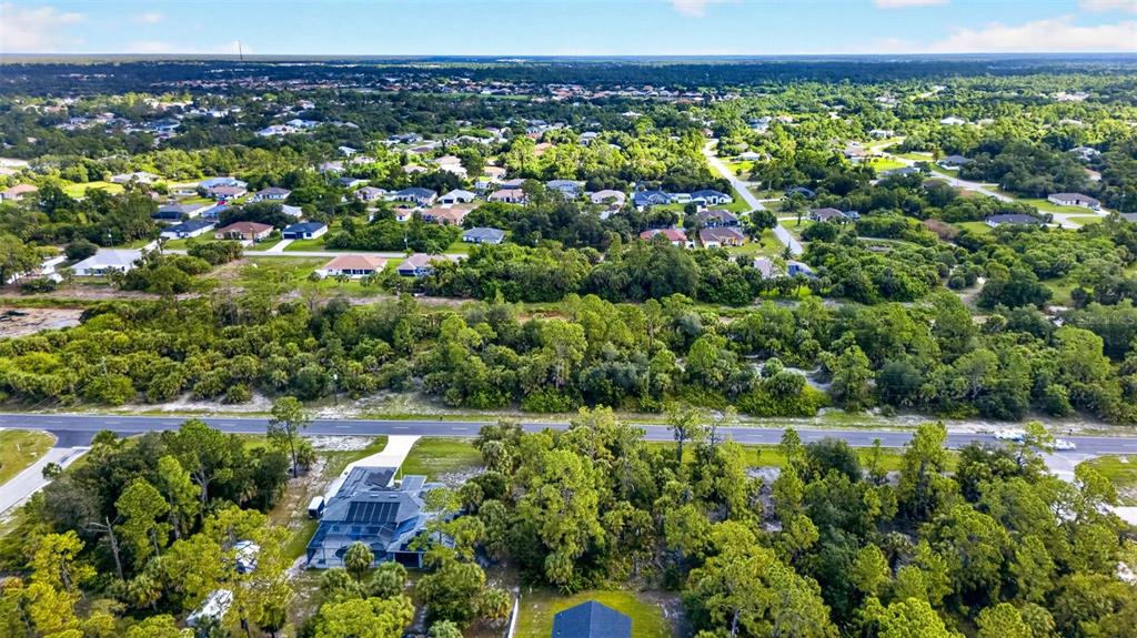 An aerial view shows a house surrounded by dense trees near a road and neighborhood — 18303 HILLSBOROUGH BOULEVARD, PORT CHARLOTTE, FL