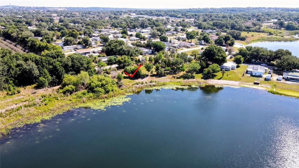 An aerial view shows a vacant lot marked with a red arrow beside a lake — 1100 PENINSULAR DRIVE, LAKE WALES, FL