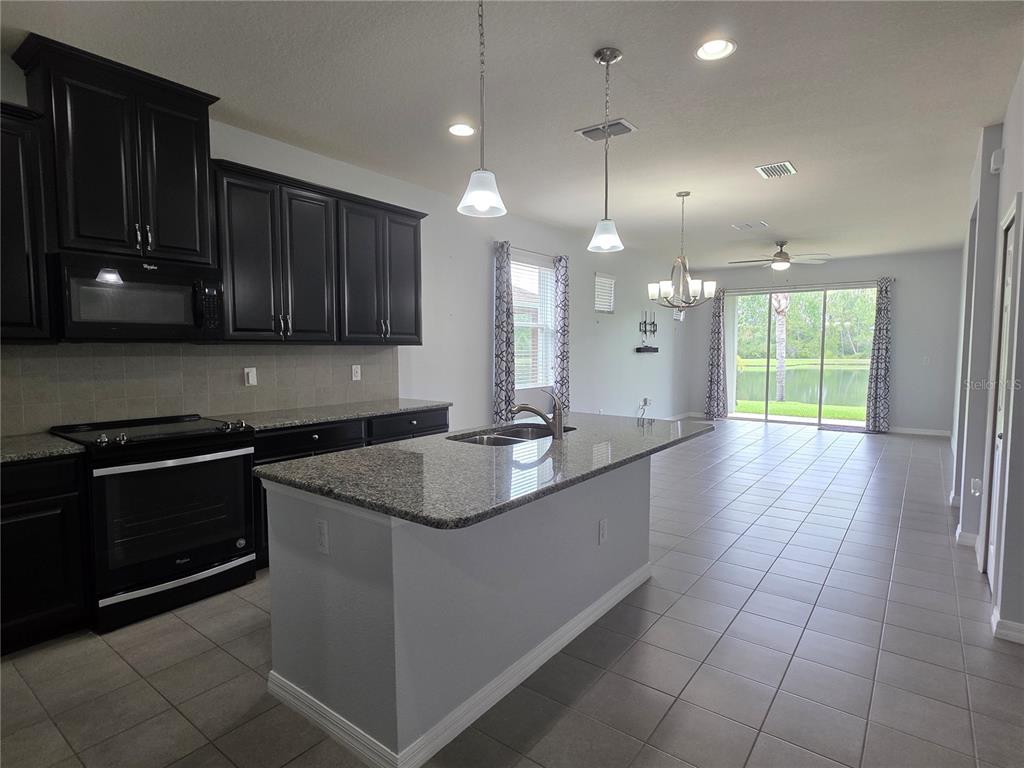 A kitchen with dark cabinets, granite countertops, and an island overlooking a living area — 4939 AUTUMN RIDGE DRIVE, WESLEY CHAPEL, FL