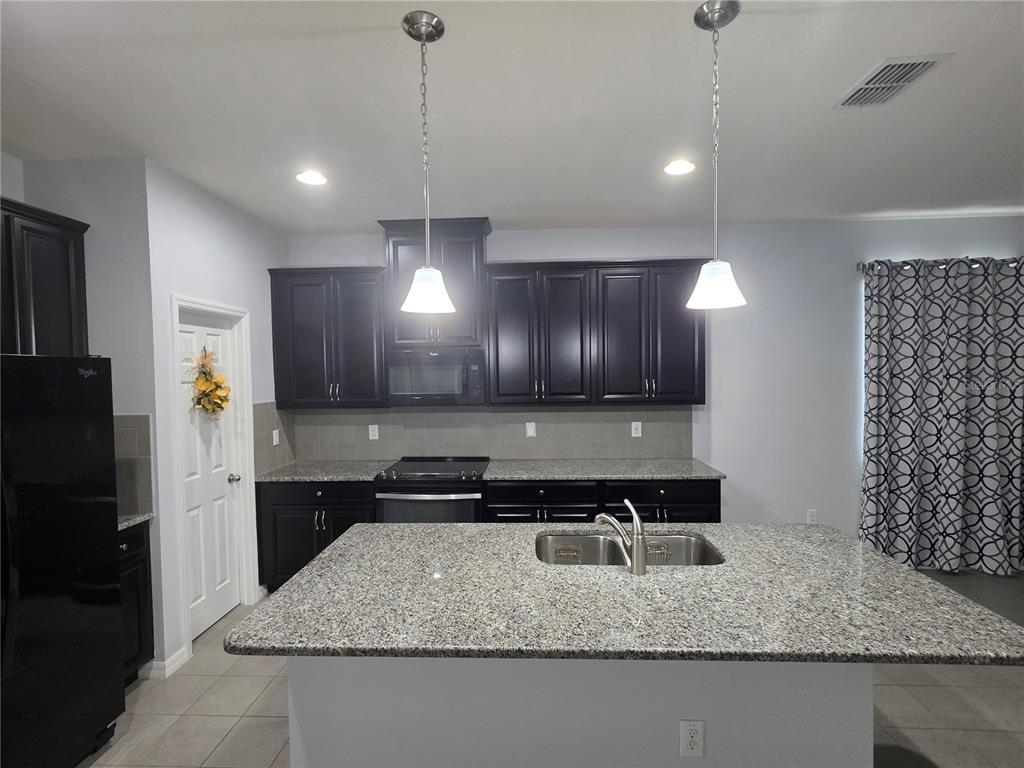 A kitchen features dark cabinetry, granite countertops, a central island with a sink, and pendants — 4939 AUTUMN RIDGE DRIVE, WESLEY CHAPEL, FL