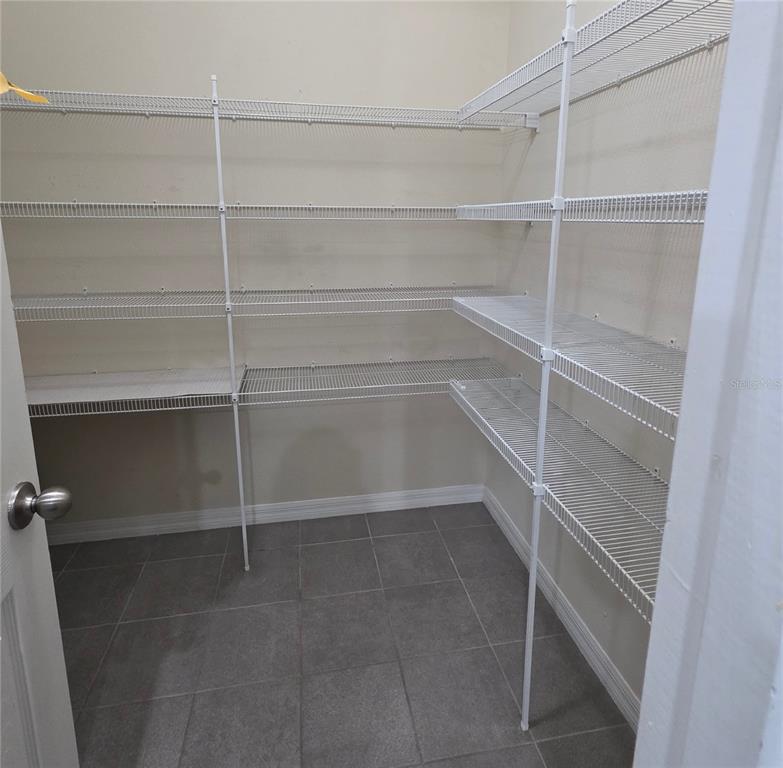A walk-in pantry features white wire shelving units installed against the walls over tiled flooring — 4939 AUTUMN RIDGE DRIVE, WESLEY CHAPEL, FL