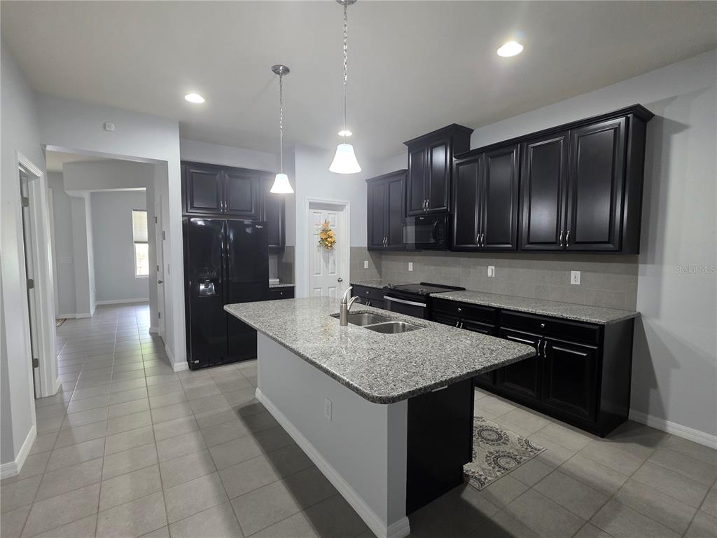 A kitchen features dark cabinets, granite countertops, a central island, and light tile flooring — 4939 AUTUMN RIDGE DRIVE, WESLEY CHAPEL, FL