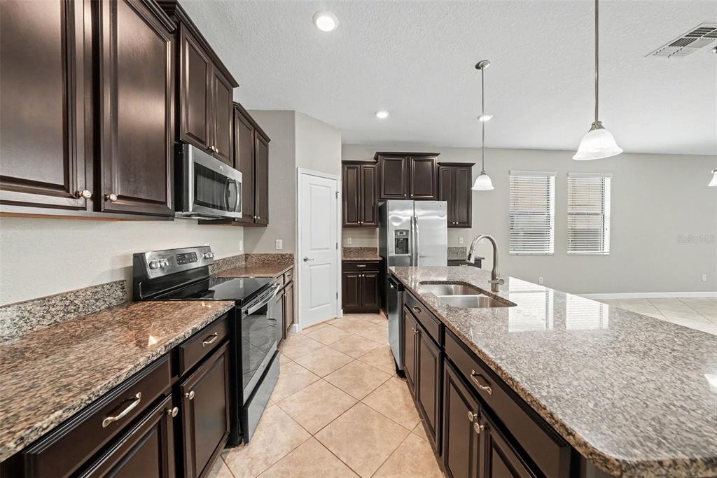 A kitchen features dark wood cabinets, granite countertops, stainless steel appliances, and tile flooring — 28500 PLEASANT BAY LOOP, WESLEY CHAPEL, FL