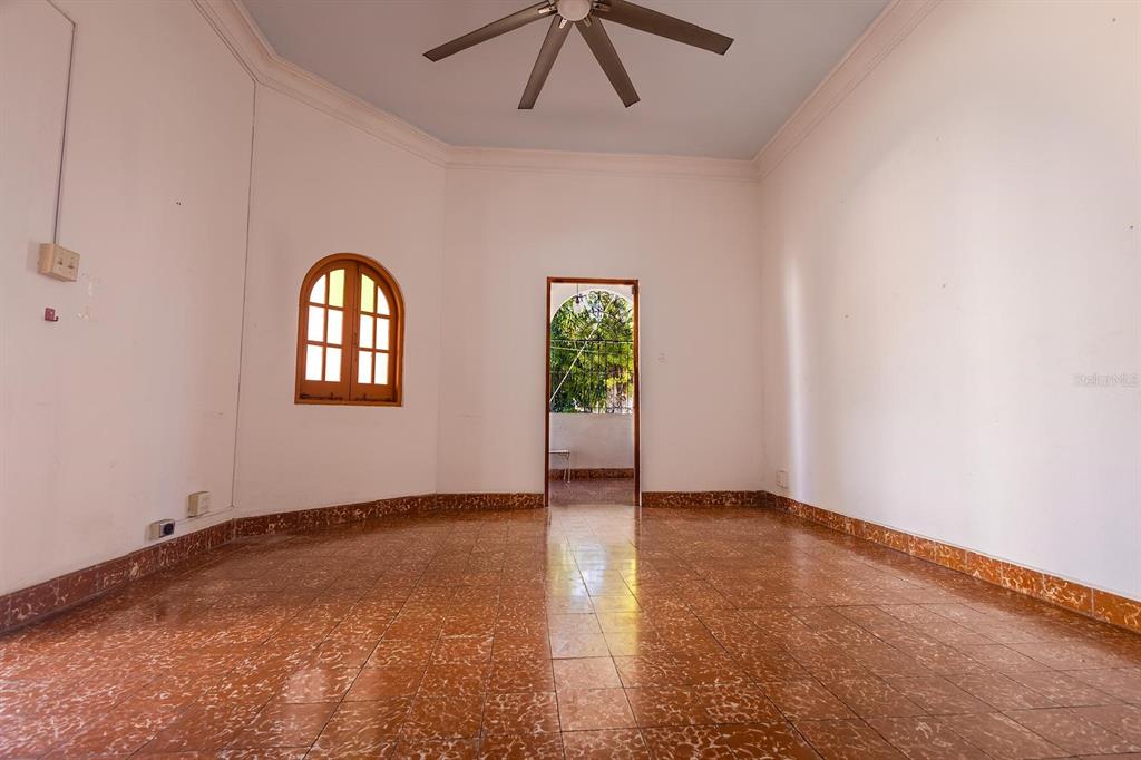 An empty room features reddish-brown tiled floors, white walls, an arched window, and a ceiling fan — 70 Calle DEL BOSQUE, MAYAGUEZ, PR