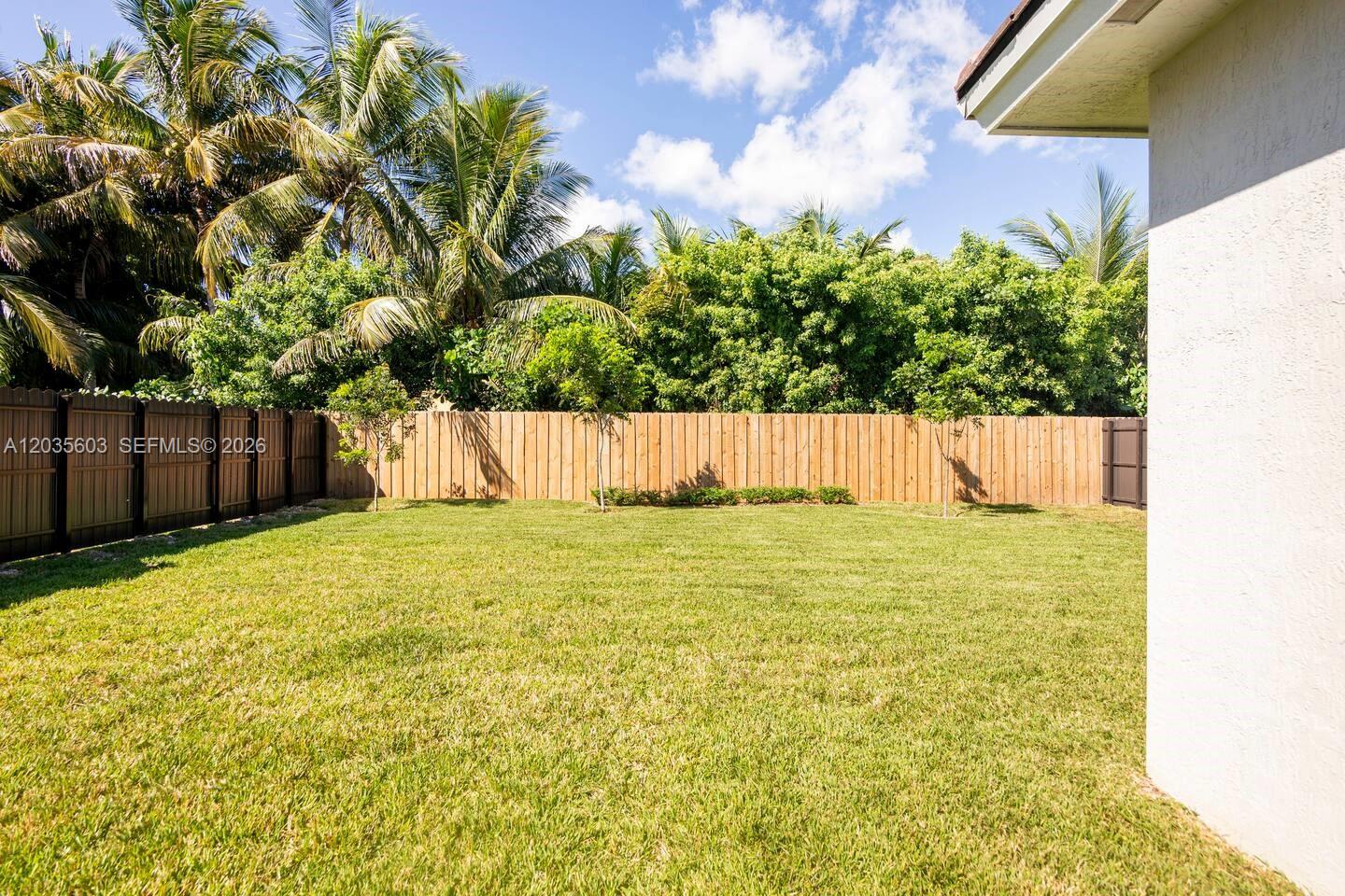 A grassy backyard features a wooden privacy fence, several small trees, and palm trees — 19452 SW 124th Ct # 0, Miami FL 33177, MIAMI, FL
