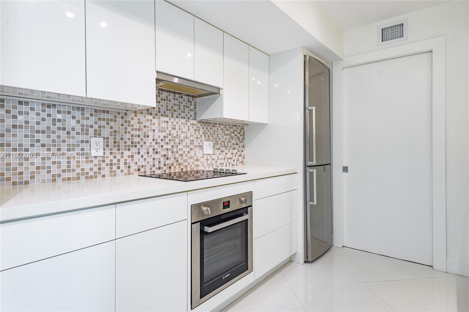 A modern kitchen features white flat-panel cabinets, stainless steel appliances, and a mosaic tile backsplash — 6917 Collins Ave # 720, Miami Beach FL 33141, MIAMI BEACH, FL
