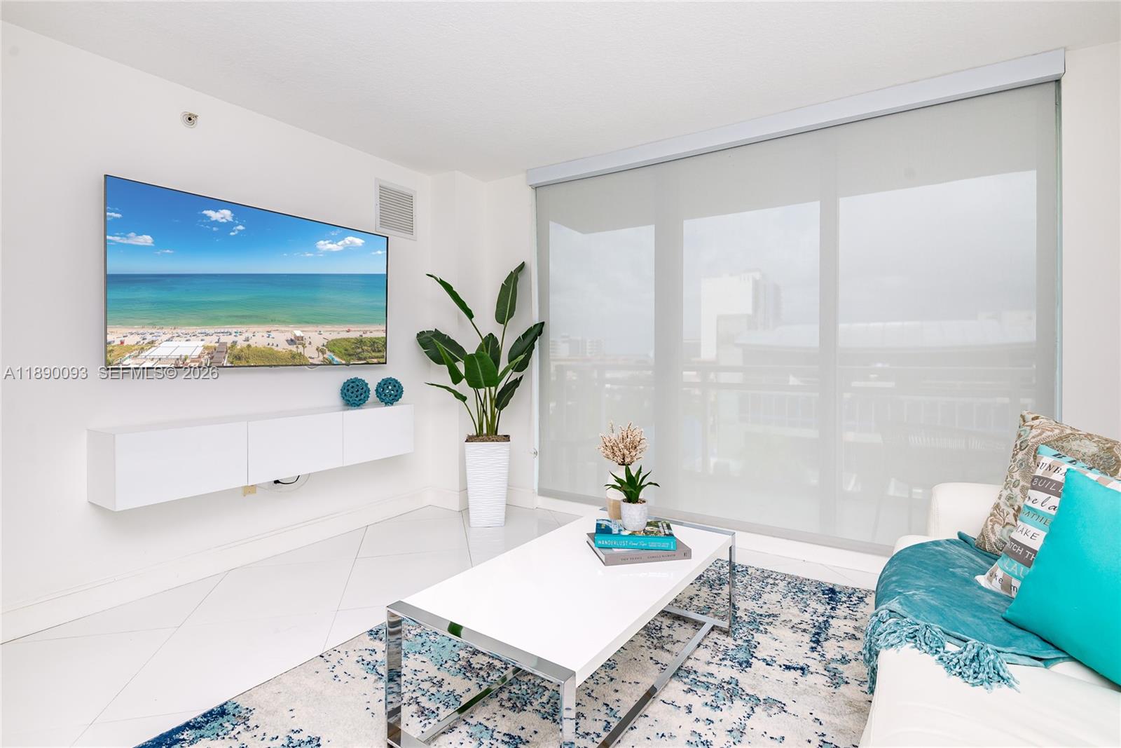 A modern living room features a wall-mounted television, white floating console, and large window blinds — 6917 Collins Ave # 720, Miami Beach FL 33141, MIAMI BEACH, FL