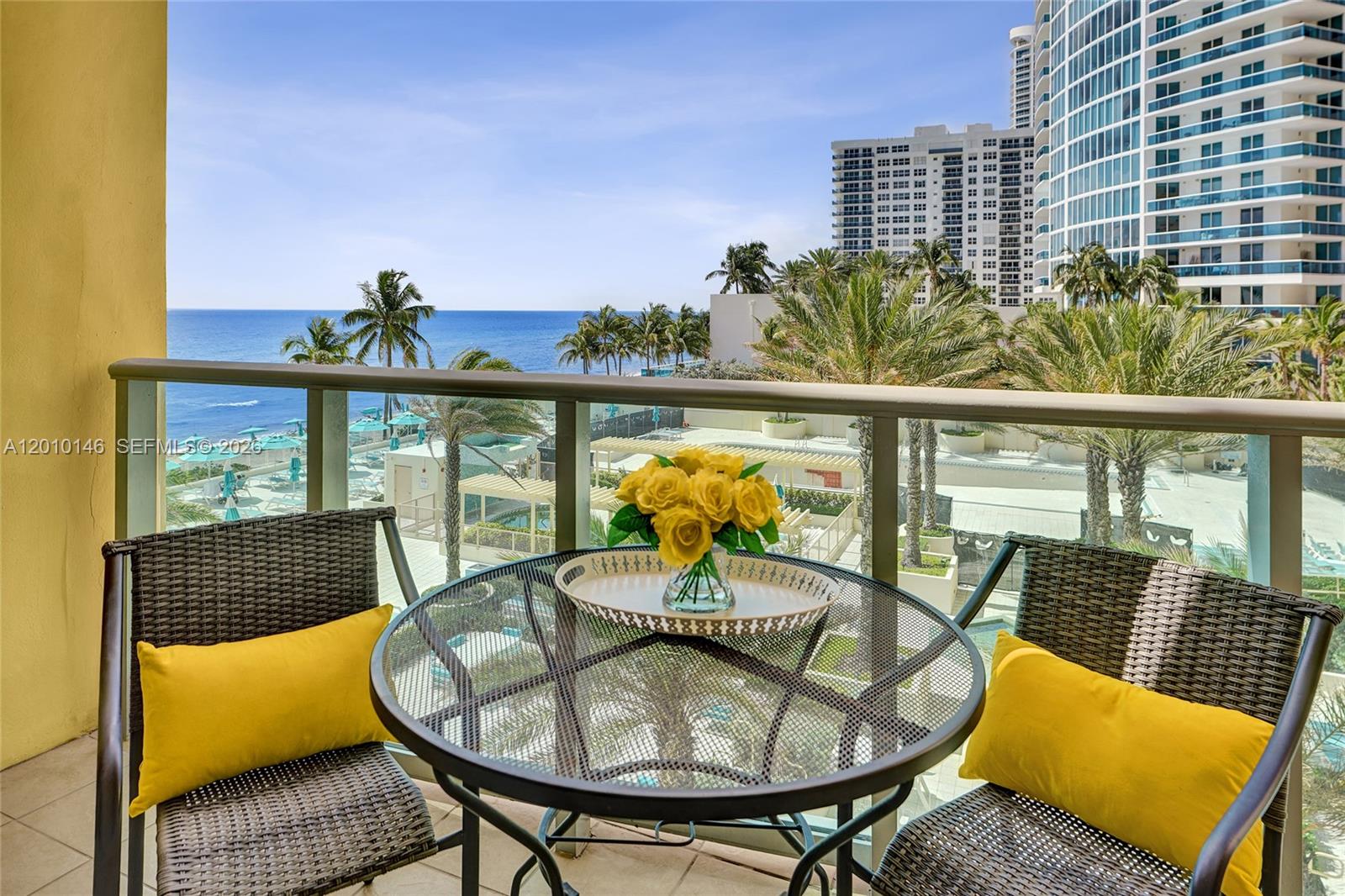A balcony features a glass-topped table with yellow flowers and two chairs overlooking the ocean — 2501 S Ocean Dr # 414, Hollywood FL 33019, HOLLYWOOD, FL