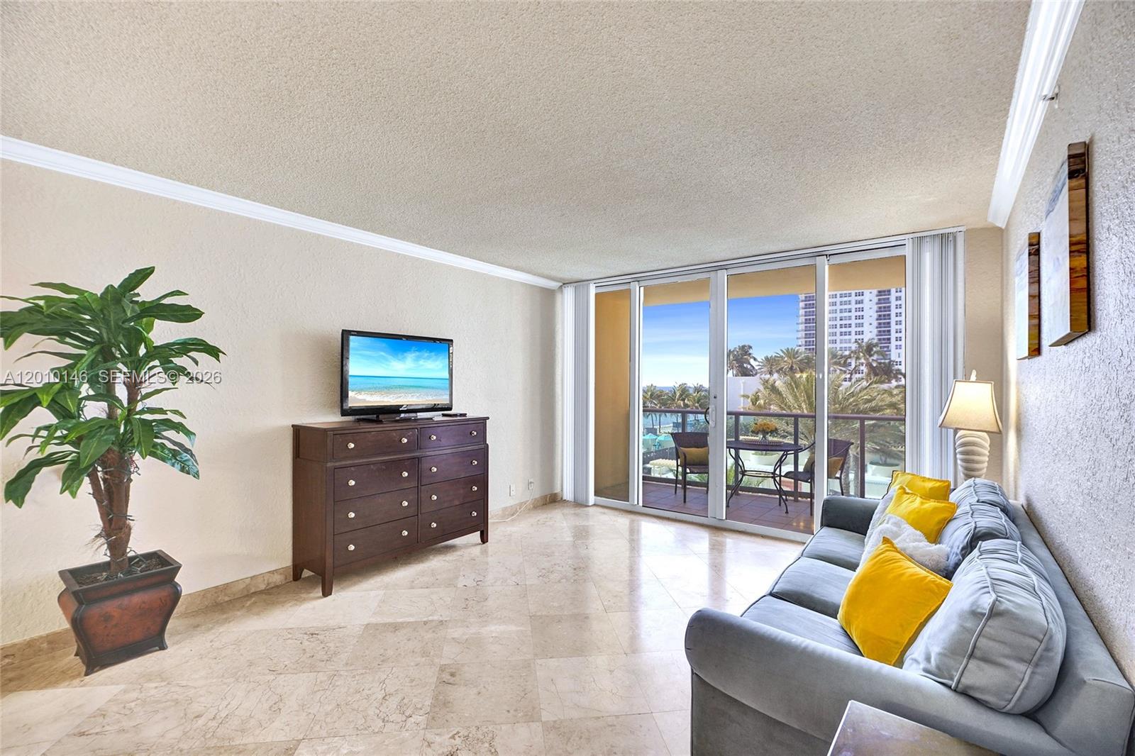A living room features a sofa, a dresser with a television, and a balcony view — 2501 S Ocean Dr # 414, Hollywood FL 33019, HOLLYWOOD, FL