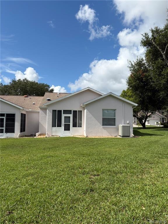 The rear exterior of a light-colored house features a screened-in porch and a central air unit — 6821 E QUEENSBURY LANE, INVERNESS, FL