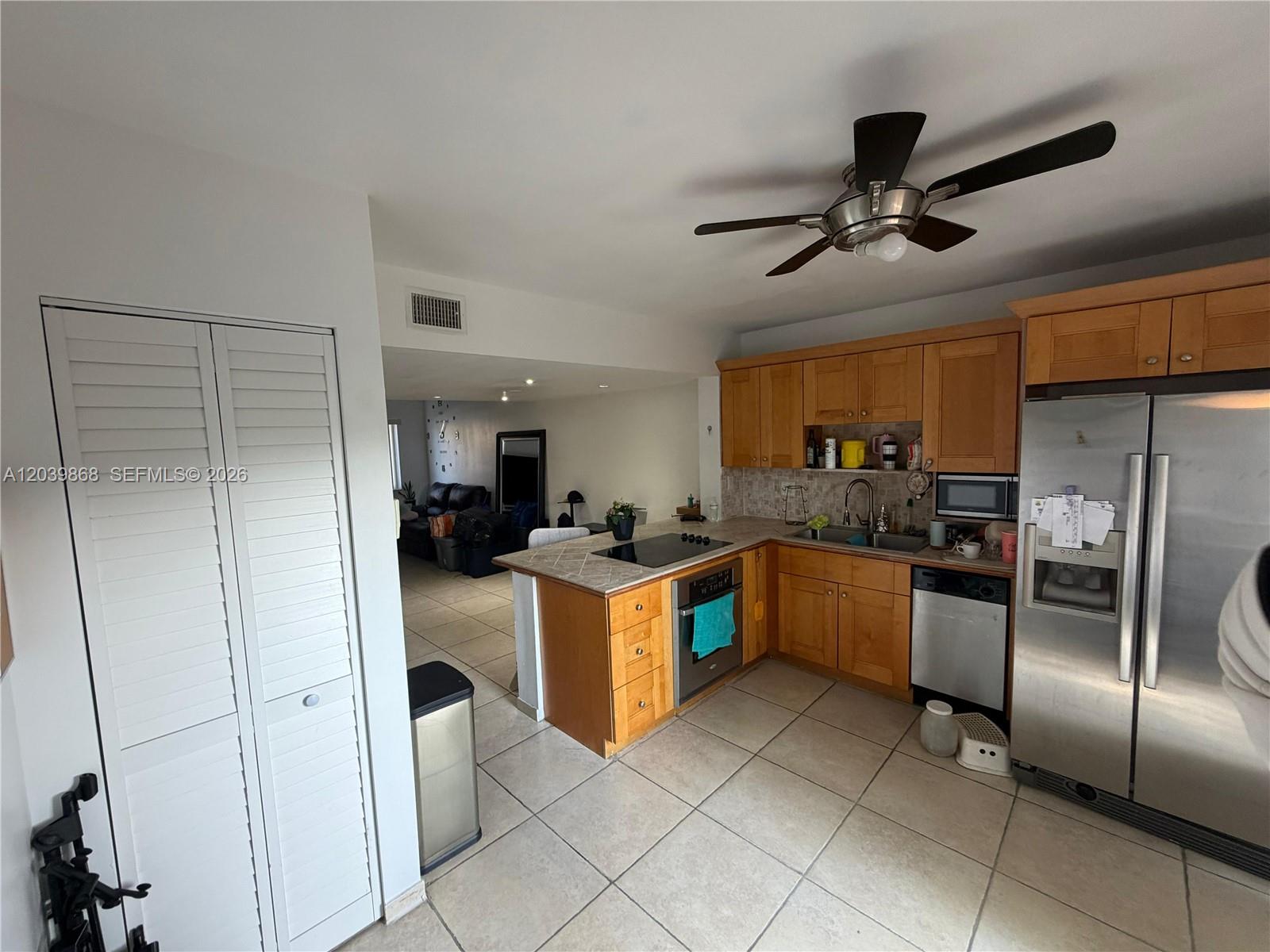 A kitchen with wood cabinets, stainless steel appliances, and tile flooring opens to a living area — 541 NW 82nd Ct # 375, Miami FL 33126, MIAMI, FL