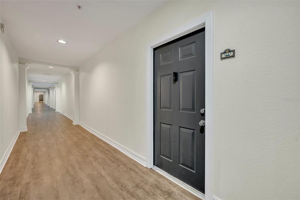 A long hallway with light-colored walls and wood-look flooring features a dark gray apartment door — 5550 E MICHIGAN STREET UNIT 2232, ORLANDO, FL