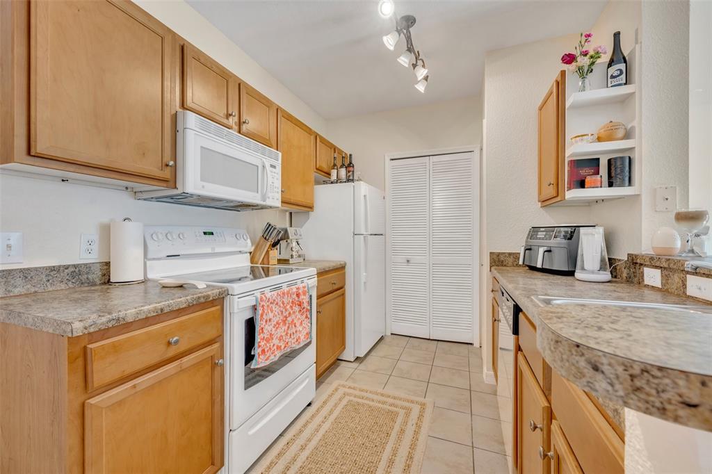 A galley kitchen features wood cabinets, laminate countertops, white appliances, and a tiled floor — 5550 E MICHIGAN STREET UNIT 2232, ORLANDO, FL