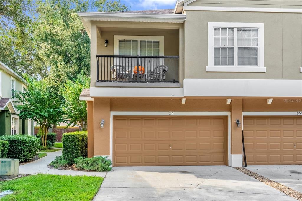 A two-story townhouse exterior features a tan garage, a balcony with seating, and white trim — 910 ASHWORTH OVERLOOK DRIVE UNIT A, APOPKA, FL
