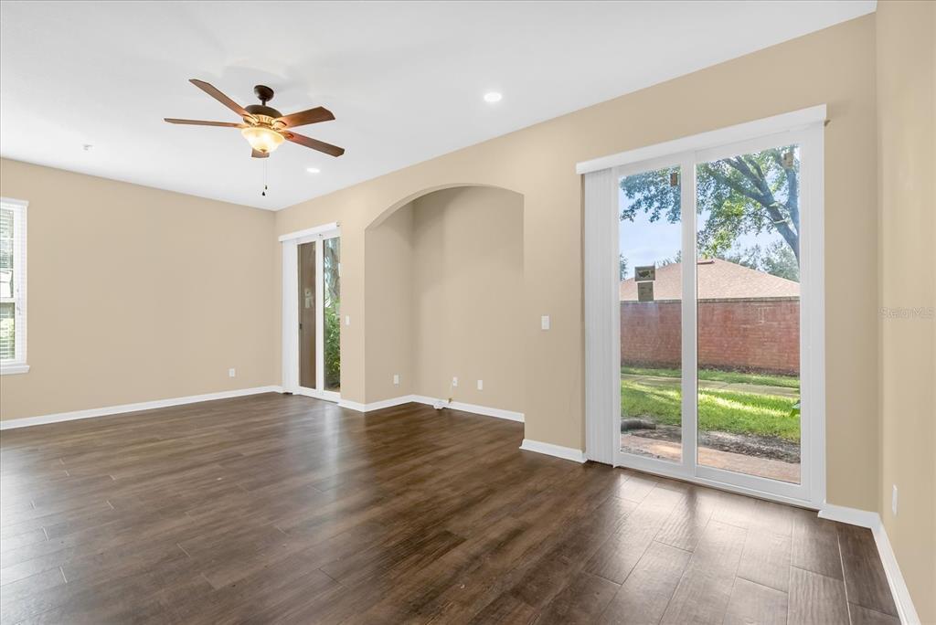 An empty room features dark wood-look flooring, beige walls, a ceiling fan, and sliding glass doors — 910 ASHWORTH OVERLOOK DRIVE UNIT A, APOPKA, FL