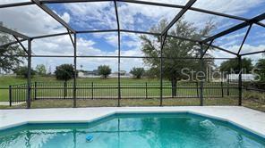 A swimming pool sits inside a screened-in patio enclosure next to a yellow house — 216 VERDI STREET, DAVENPORT, FL