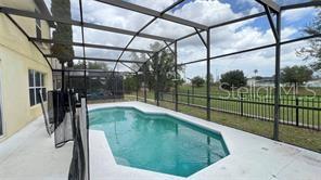 A swimming pool enclosed by a screened lanai overlooks a grassy yard and distant houses — 216 VERDI STREET, DAVENPORT, FL