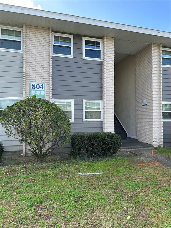 The exterior of a two-story apartment building features gray siding, brick columns, and a staircase — 804 SKY LAKE CIRCLE UNIT B, ORLANDO, FL