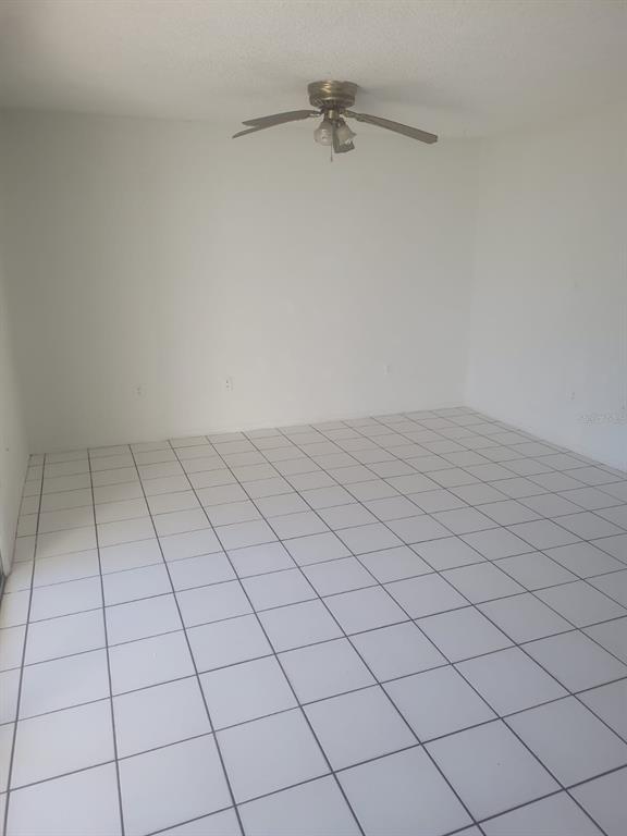 An empty room features white tiled flooring, plain white walls, and a ceiling fan — 804 SKY LAKE CIRCLE UNIT B, ORLANDO, FL