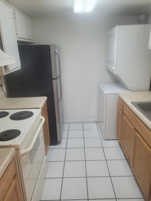 A kitchen features white tile flooring, wooden cabinets, a black refrigerator, and a stacked washer-dryer — 804 SKY LAKE CIRCLE UNIT B, ORLANDO, FL