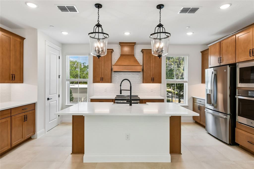 A kitchen features wood cabinets, a white island, stainless steel appliances, and two hanging lanterns — 194 PASQUALA, OVIEDO, FL