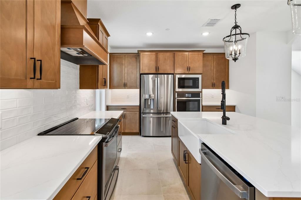 A modern kitchen features wood cabinets, stainless steel appliances, white countertops, and a farmhouse sink — 194 PASQUALA, OVIEDO, FL
