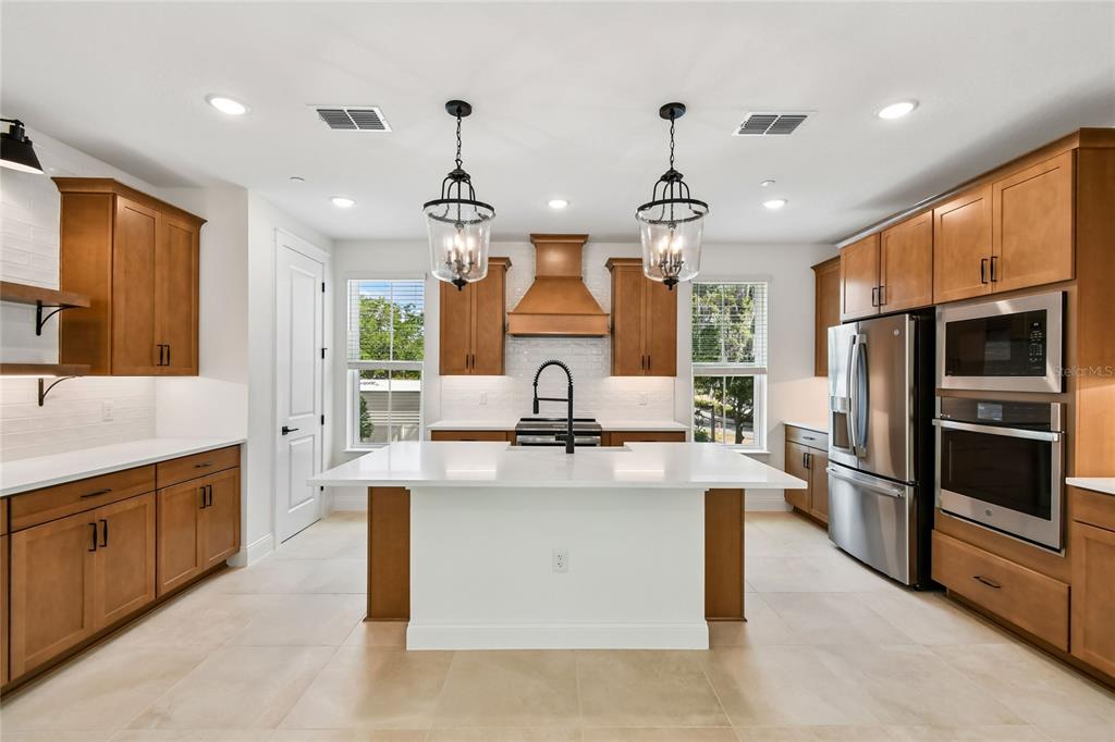 A kitchen features wood cabinets, a white island, stainless steel appliances, and two pendant lights — 194 PASQUALA, OVIEDO, FL