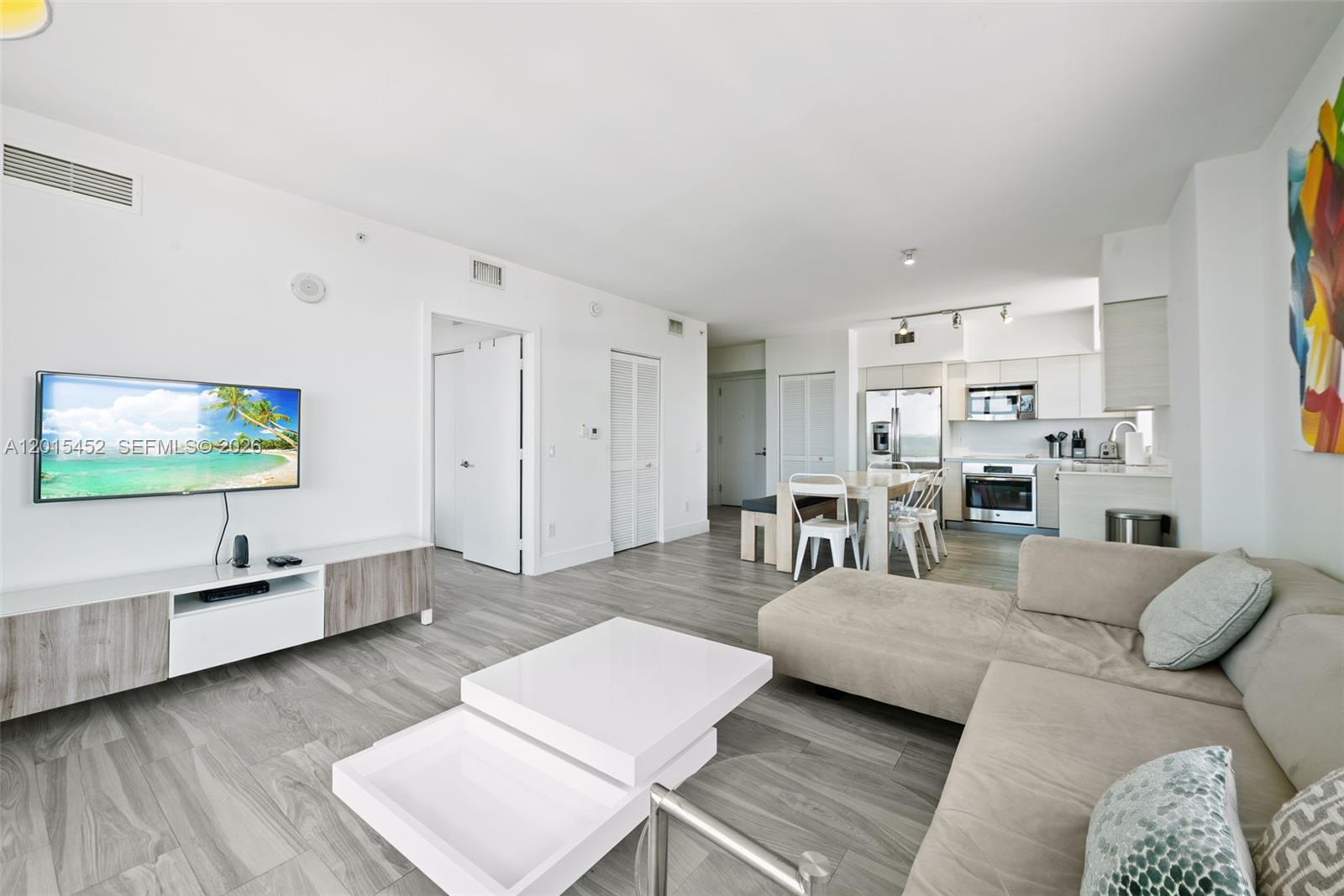 A modern open-concept living room and kitchen feature light wood flooring and white cabinetry — 4250 Biscayne Blvd # 1009, Miami FL 33137, MIAMI, FL