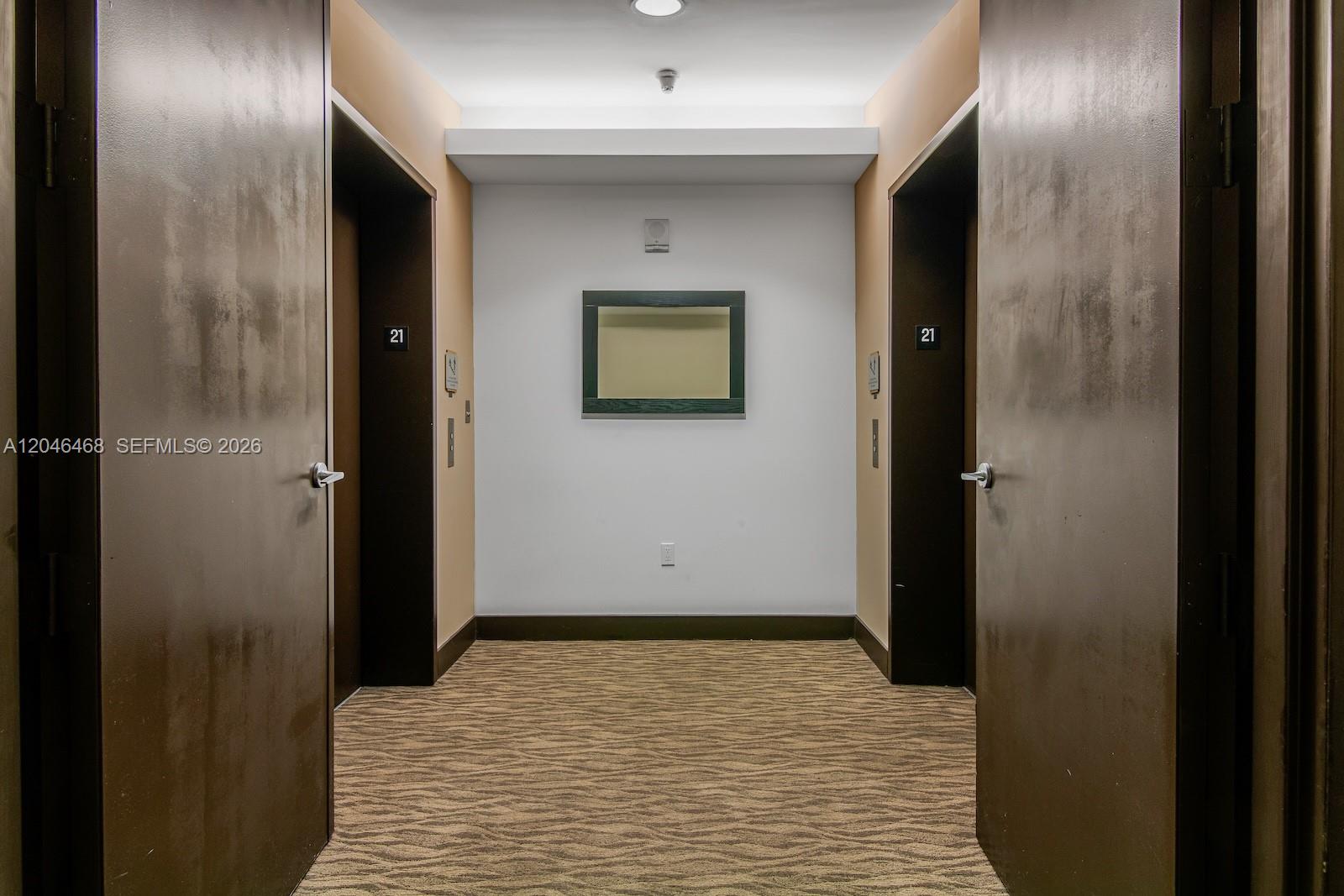 A hallway features two dark elevator doors labeled 21, a central mirror, and patterned carpeting — 79 SW 12th St, Miami FL 33130, MIAMI, FL