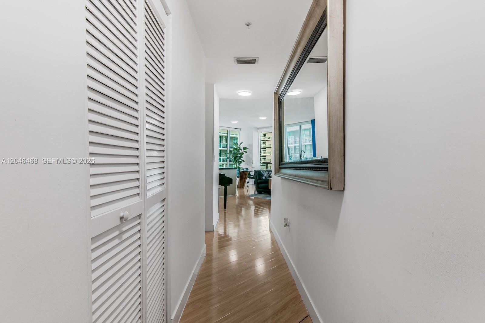 A hallway with light wood flooring, louvered closet doors, and a large wall mirror — 79 SW 12th St, Miami FL 33130, MIAMI, FL