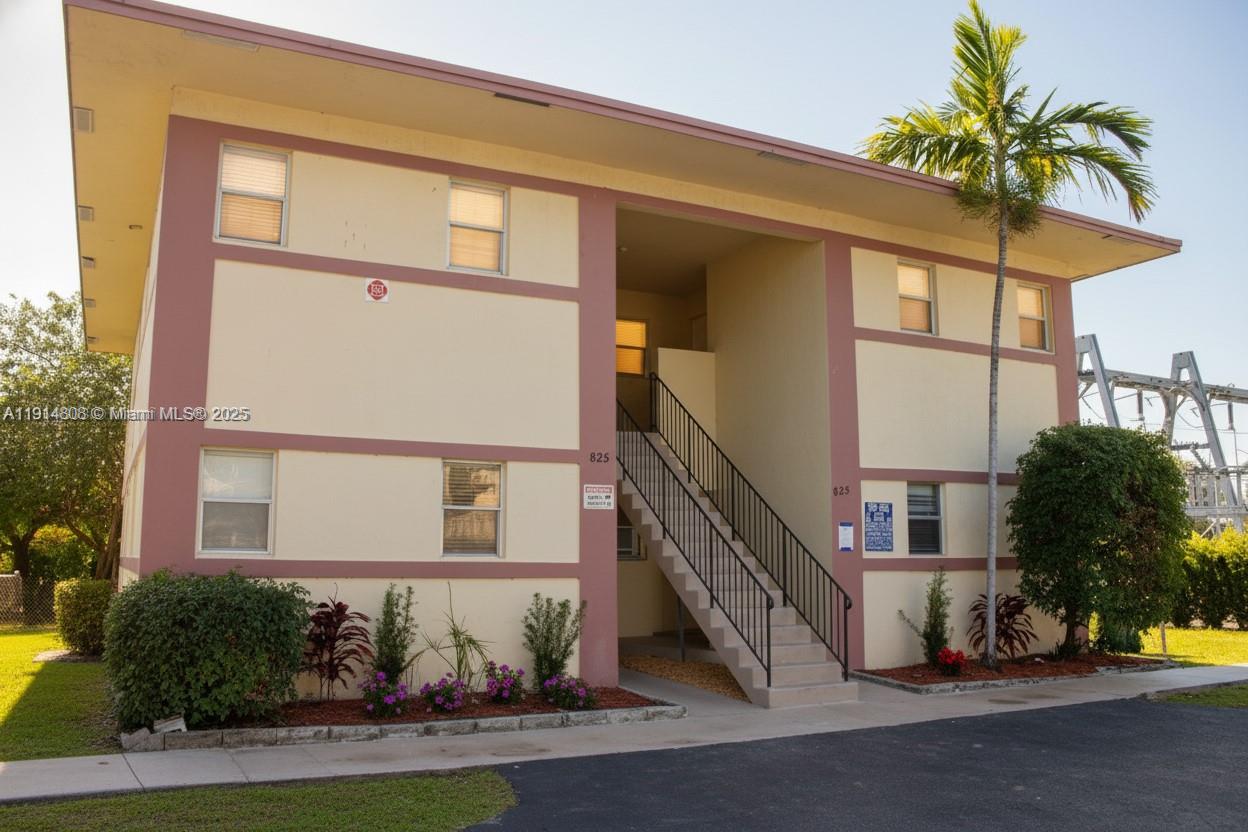 A two-story apartment building features a central outdoor staircase and a palm tree — 825 SW 10th St, Hallandale Beach FL 33009, HALLANDALE BEACH, FL