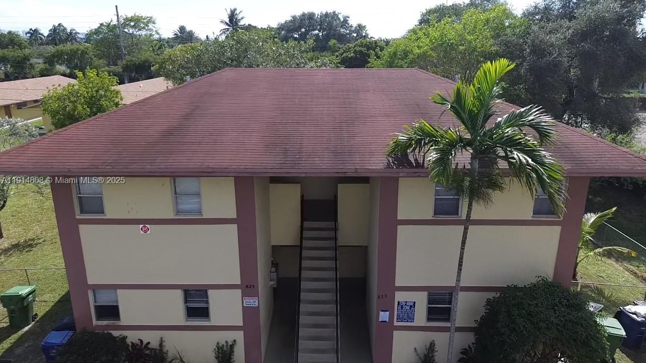 An exterior view of a two-story apartment building with a central staircase and palm tree — 825 SW 10th St, Hallandale Beach FL 33009, HALLANDALE BEACH, FL
