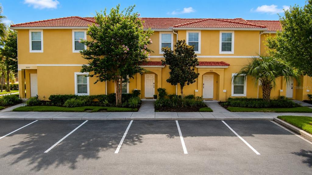 A two-story yellow townhouse complex with a red tile roof and parking spaces in front — 3003 WHITE ORCHID ROAD, KISSIMMEE, FL