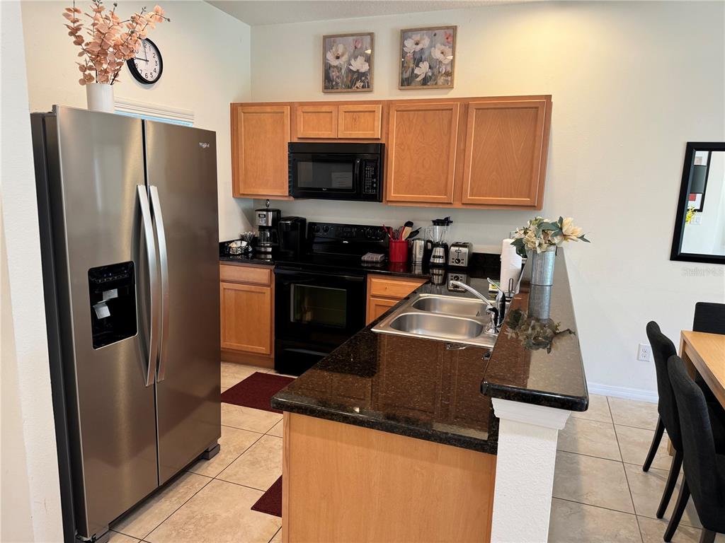 A kitchen features light wood cabinets, dark granite countertops, stainless steel appliances, and tile flooring — 3003 WHITE ORCHID ROAD, KISSIMMEE, FL
